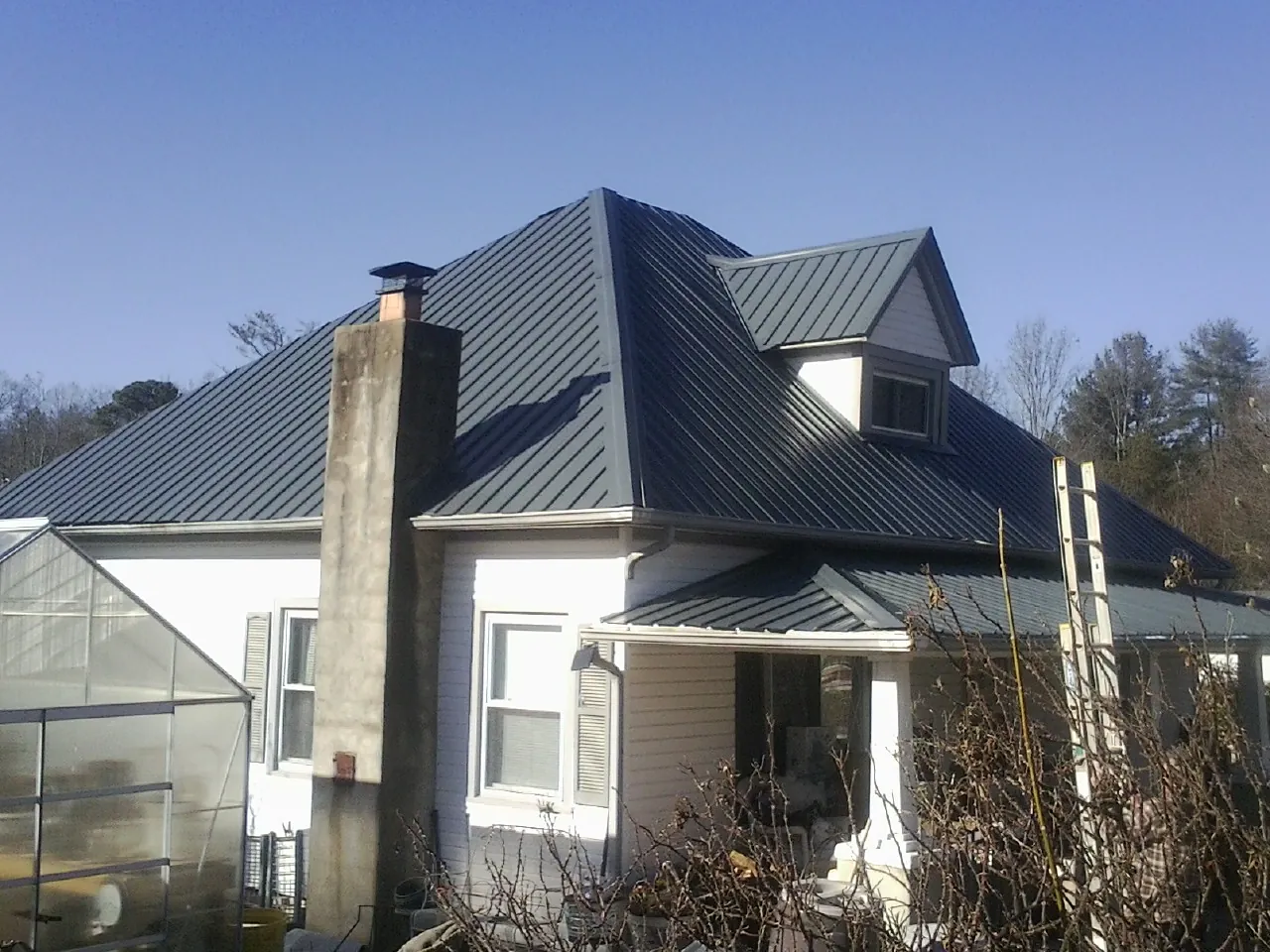 Dark blue standing seam metal roof on a white farmhouse with dormer — Slate & Tile Roof Repair by Roofing Brothers in Elbing