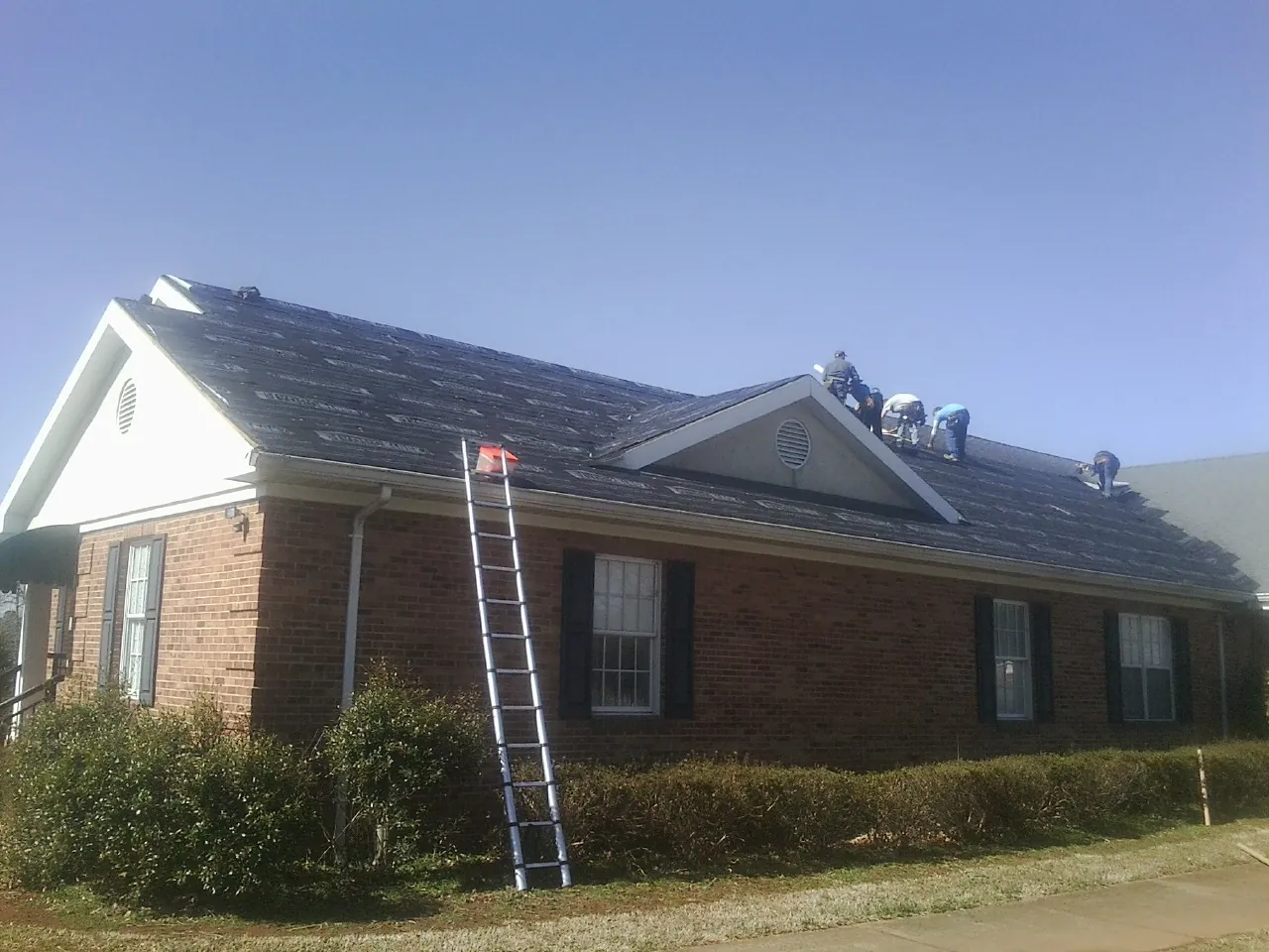 Crew tearing shingles off a brick ranch roof with a ladder set — Emergency Roof Repair work by our crew in Elbing