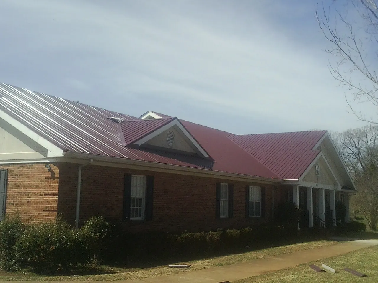 Red metal roof with gabled entries on a long brick building, from a Hail Damage Roof Repair job in Elbing