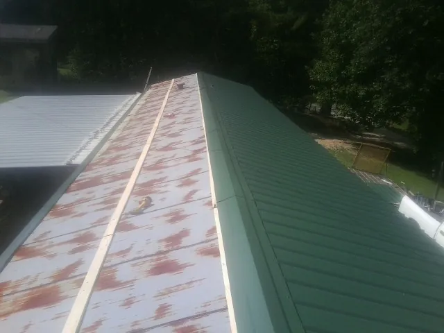 Old rusted panels beside newly installed green metal roofing — Wind Damage Roof Repair by Roofing Brothers in Elbing
