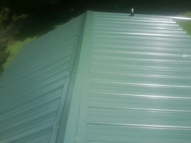 New green metal panels meeting at the ridge of a roof — Flat Roof Repair work by our crew in Elbing