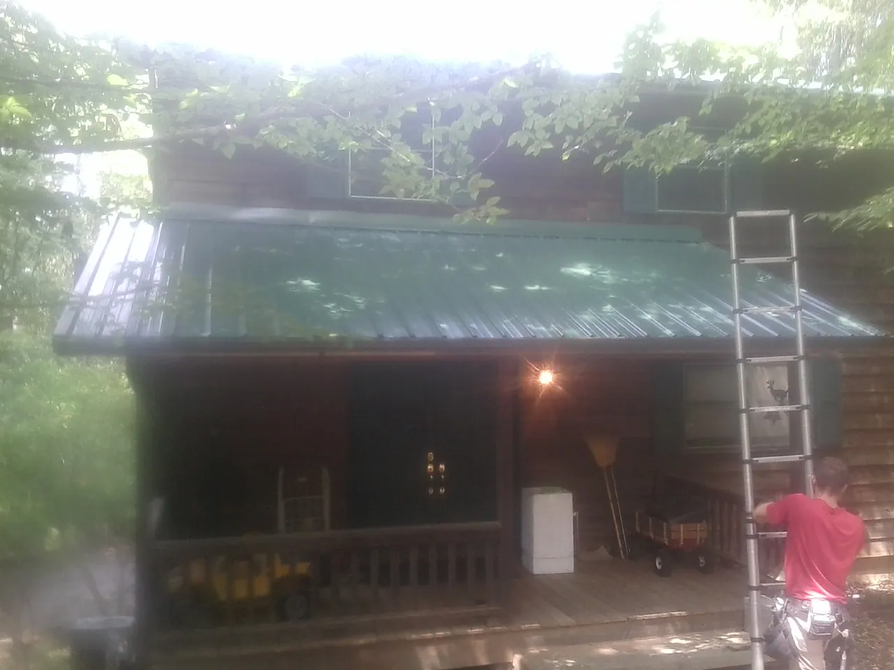 Worker on a ladder at the green porch roof of a wooded cabin in Elbing