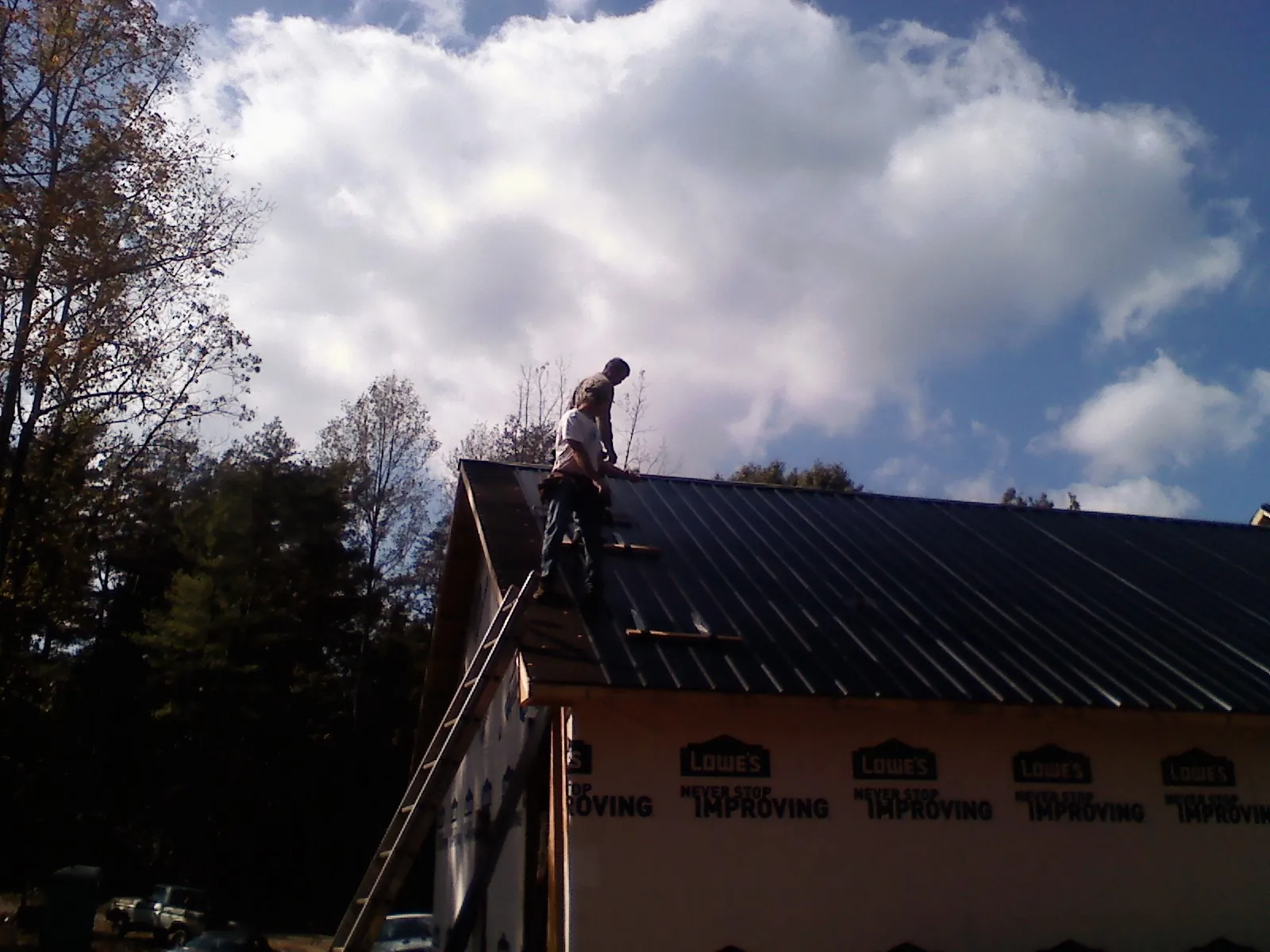 Roofer fastening dark metal panels high against a cloudy sky, from a Roof Inspection job in Elbing