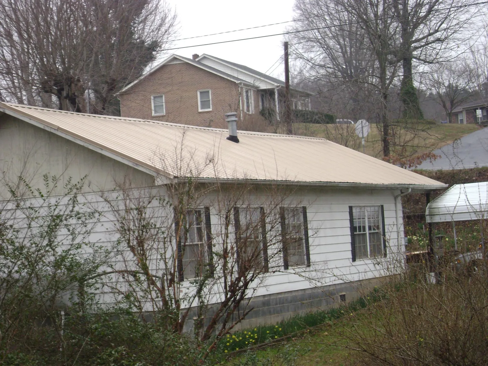 Tan metal roof on a white sided house set into a hillside — Commercial Roofing by Roofing Brothers in Elbing